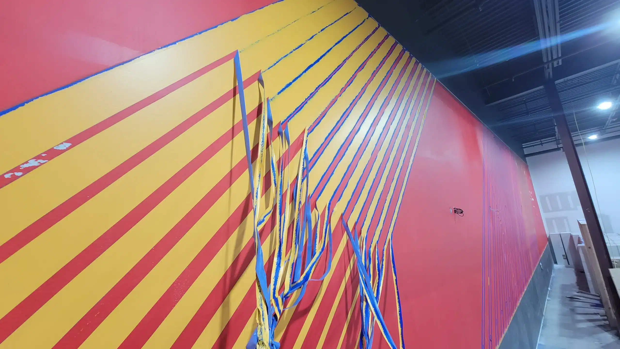 Creative Accent Wall Painting for Businesses Bold red and yellow striped accent wall with painter's tape, showcasing graphic painting.