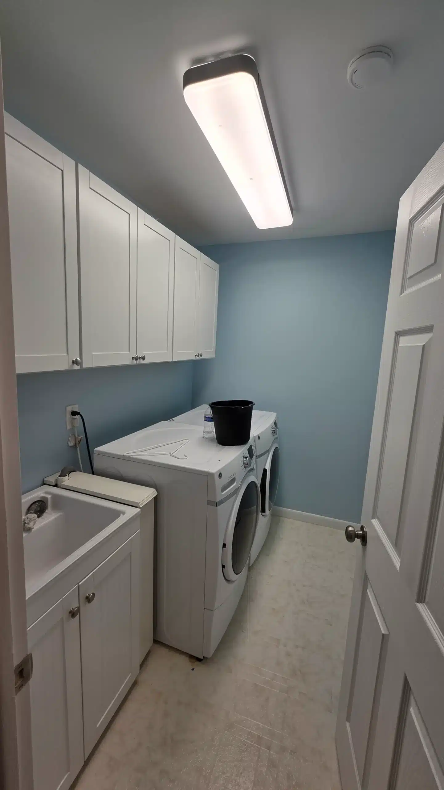 Laundry Room Interior Painting and Cabinet Refresh Clean laundry room featuring light blue painted walls, white upper and lower cabinets, and appliances, highlighting interior painting.