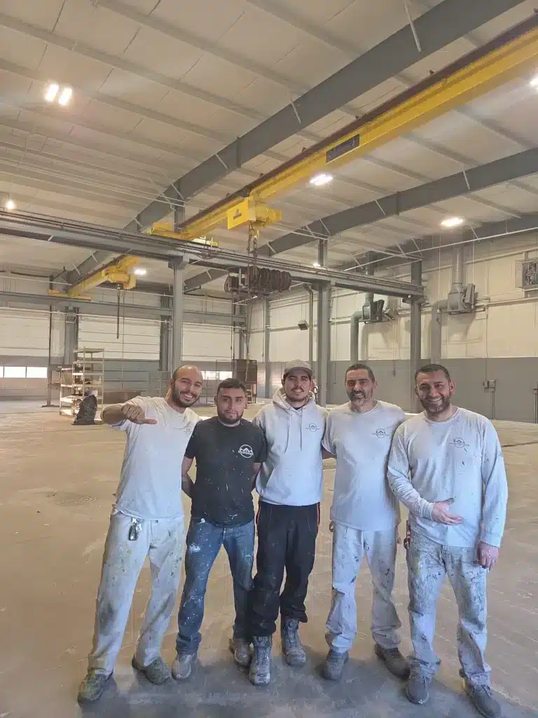 A team of five professional male painters in work clothes posing inside a large commercial building.