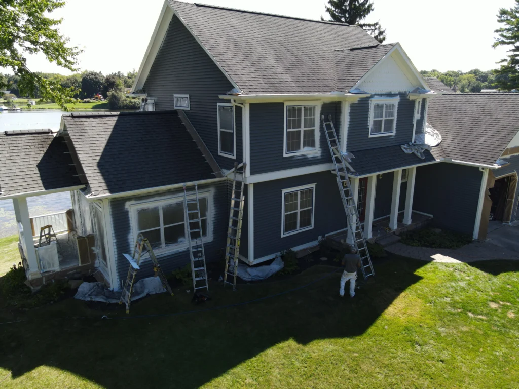 Large Lake House Exterior Painting in Progress Professional painters working on a large two story lake house with gray siding and white trim.