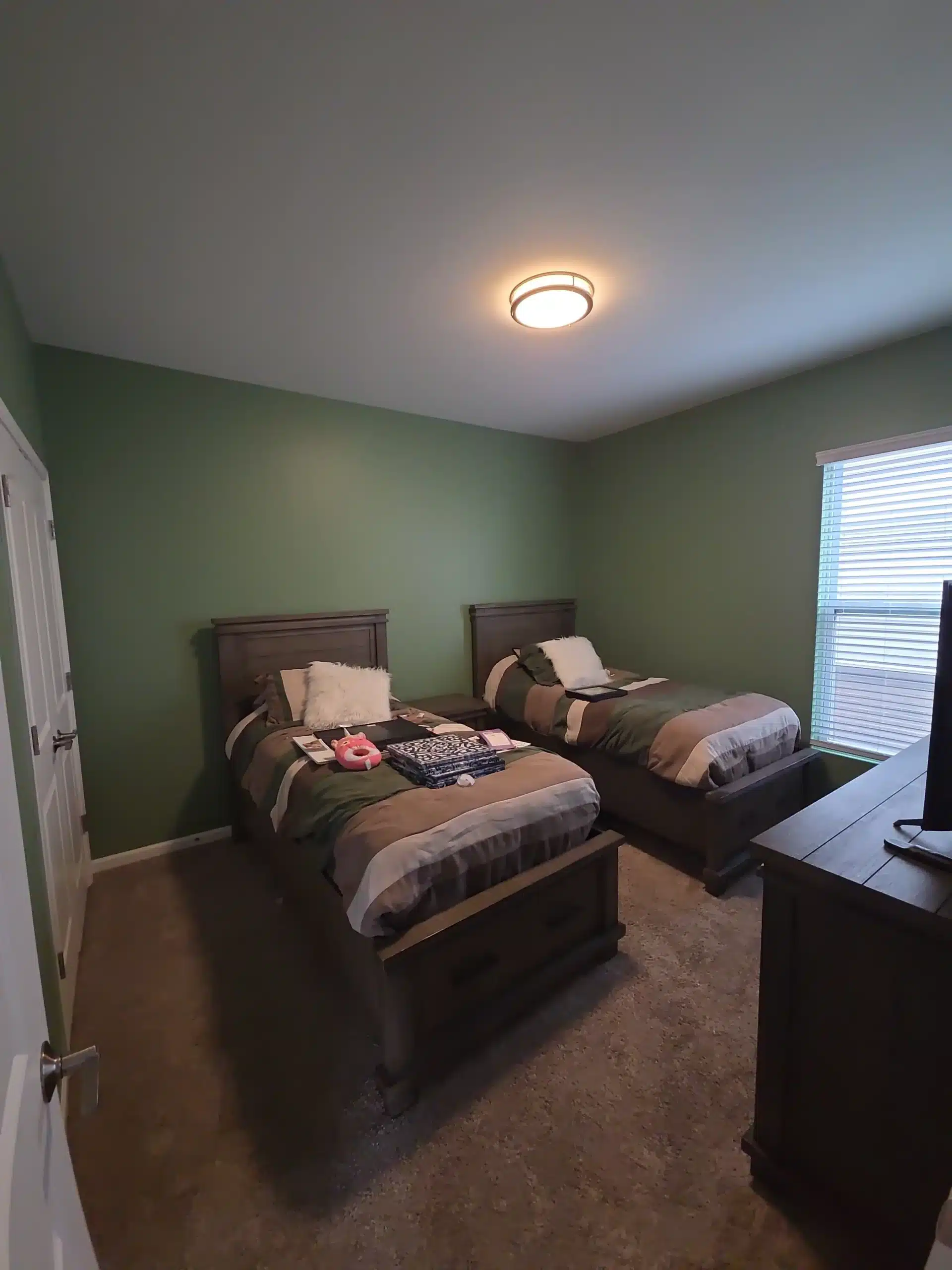 Green Bedroom Interior Painting Services A freshly painted bedroom featuring vibrant green walls, two beds, and a window, highlighting professional interior painting.