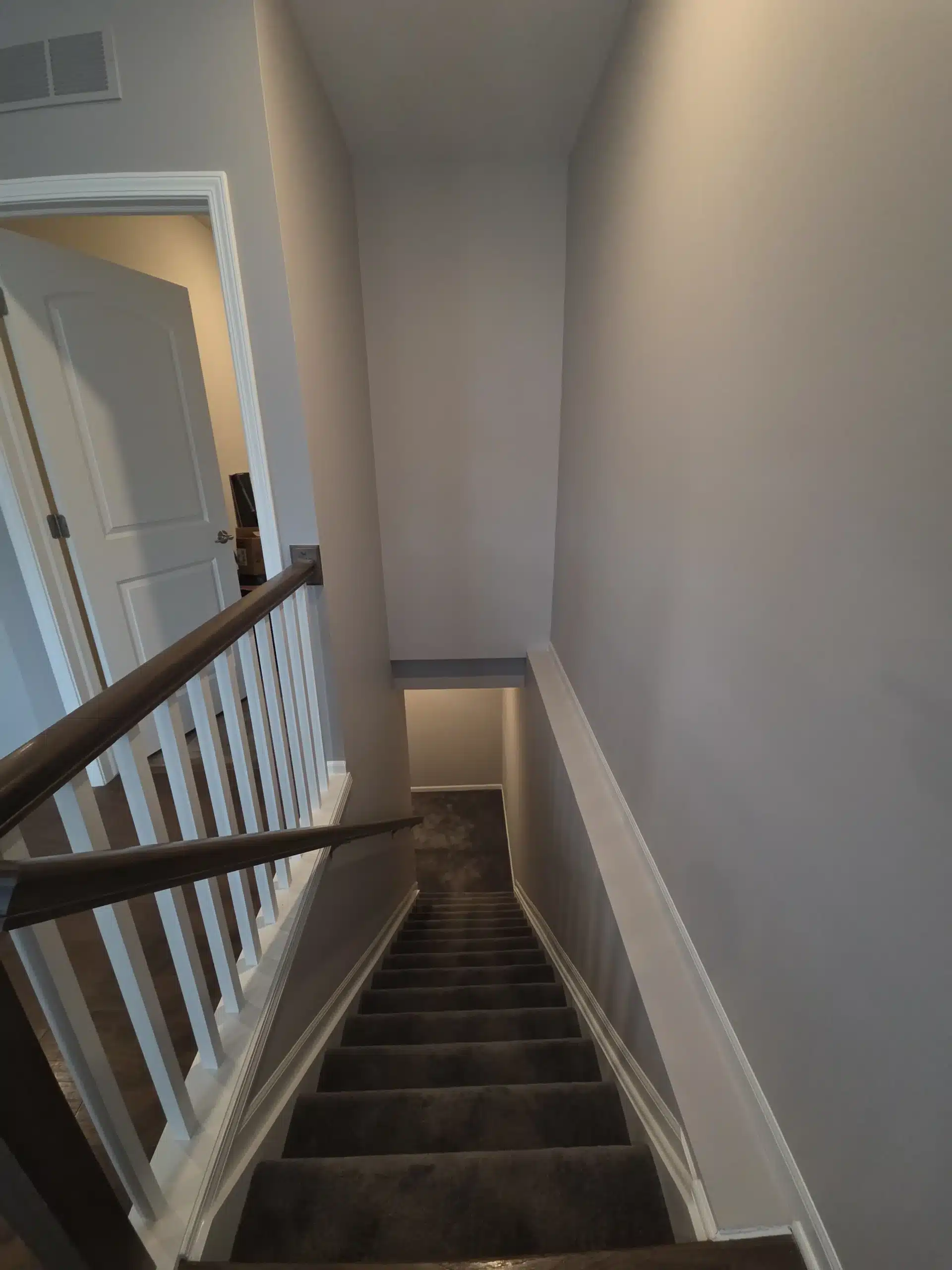 Staircase Painting with Light Gray Walls and White Trim Freshly painted staircase featuring light gray walls, crisp white trim, and a dark wood handrail.