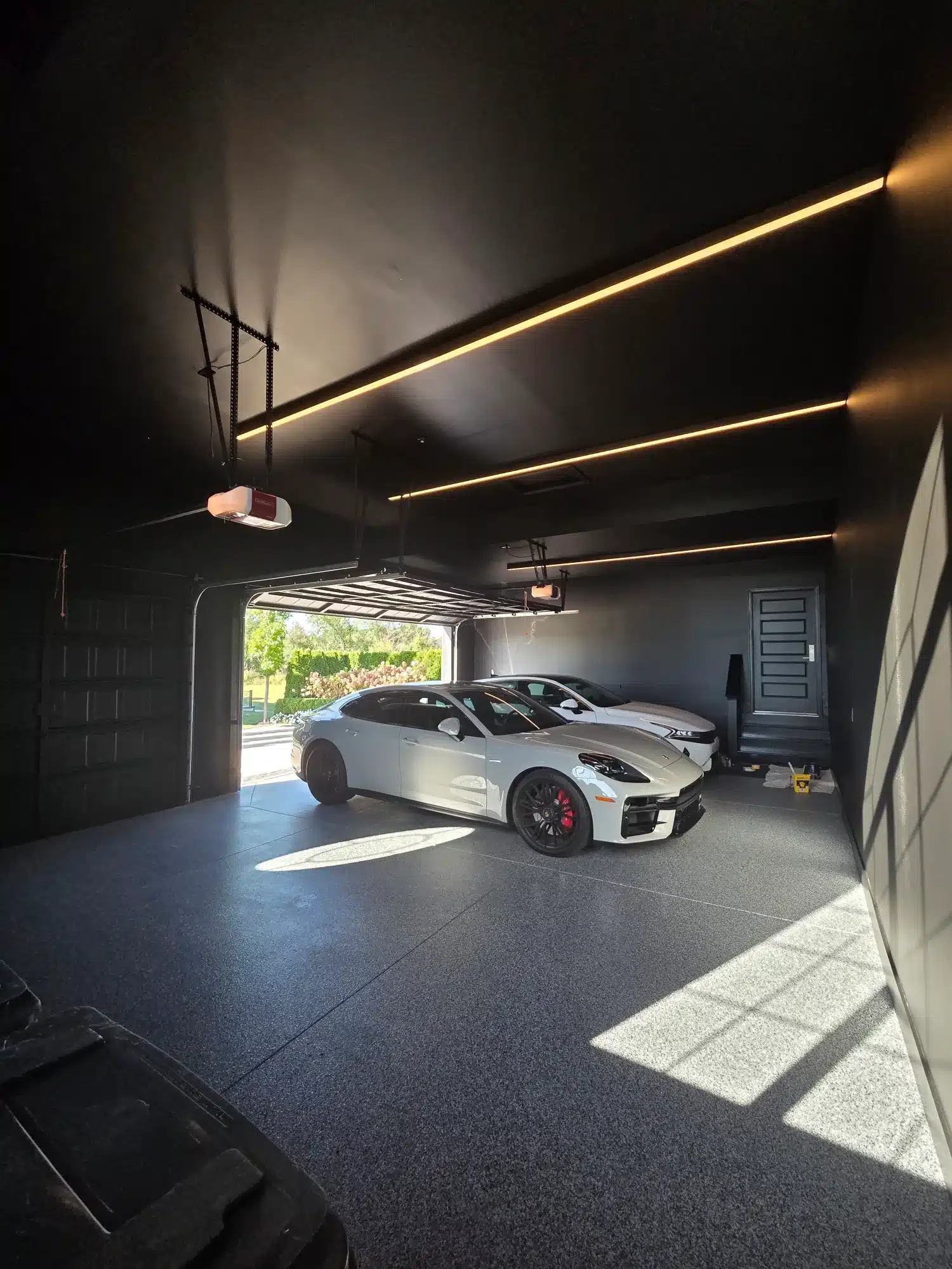 Charcoal Epoxy Garage Floor Charcoal epoxy-coated garage floor with speckled aggregate in modern garage with gold linear ceiling lights and white sports
