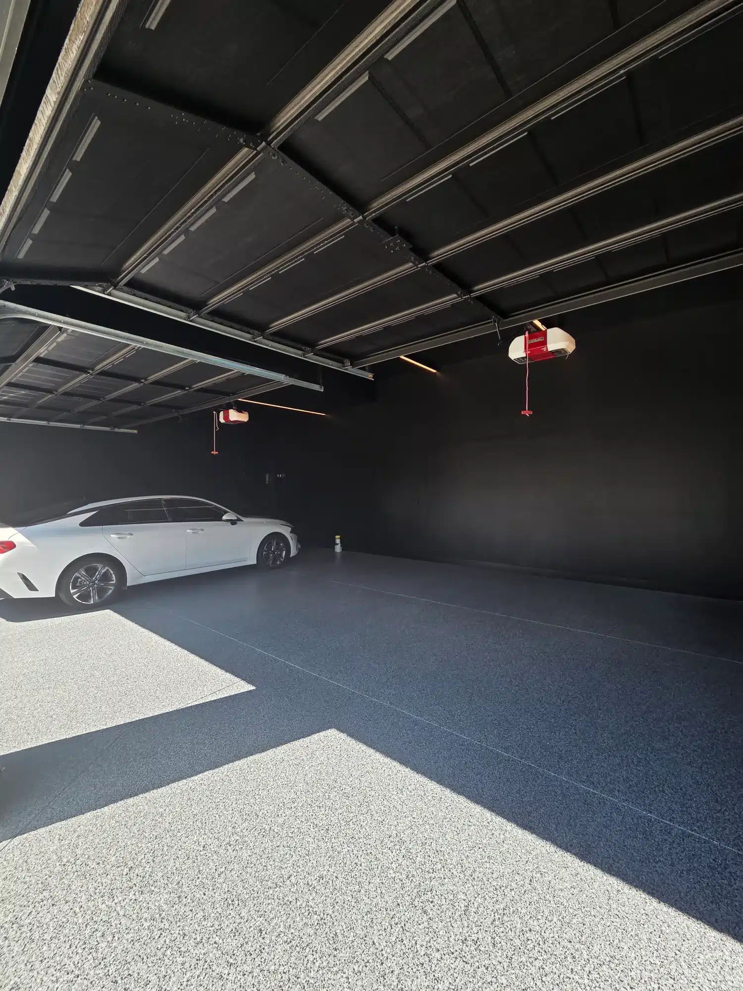 Dark Blue Epoxy Garage Floor Dark blue epoxy-coated garage floor with light aggregate flake pattern and black painted walls in modern residential garage.